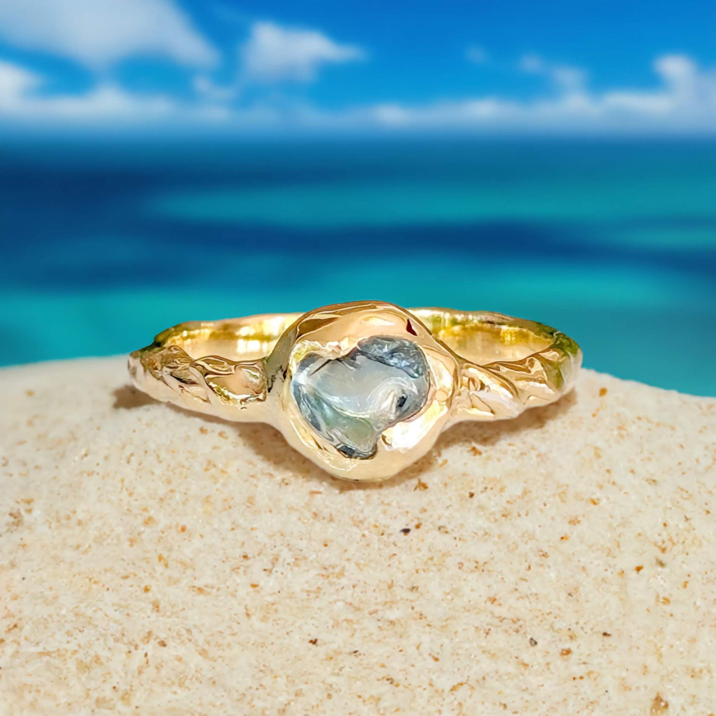 Australian sapphire ring in solid 14k gold with textured band, set against a beach backdrop.