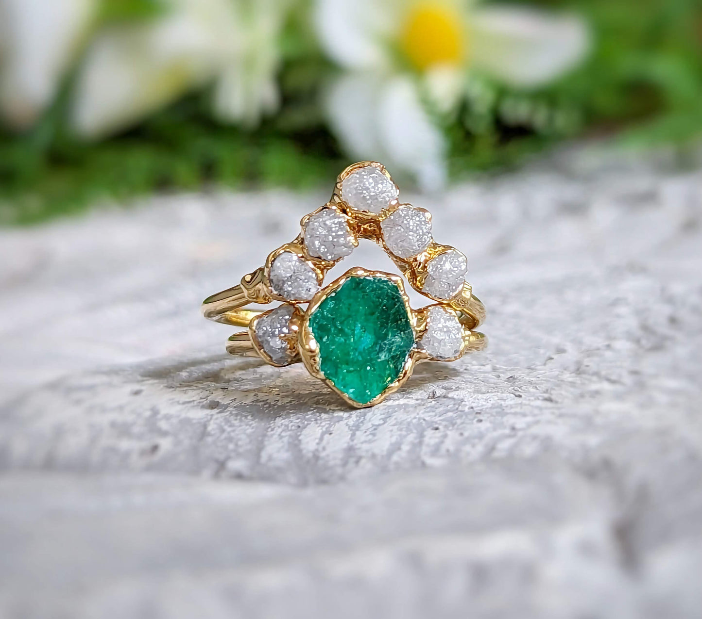 Raw emerald and diamond chevron bridal ring set on a textured surface, featuring a unique gold band.