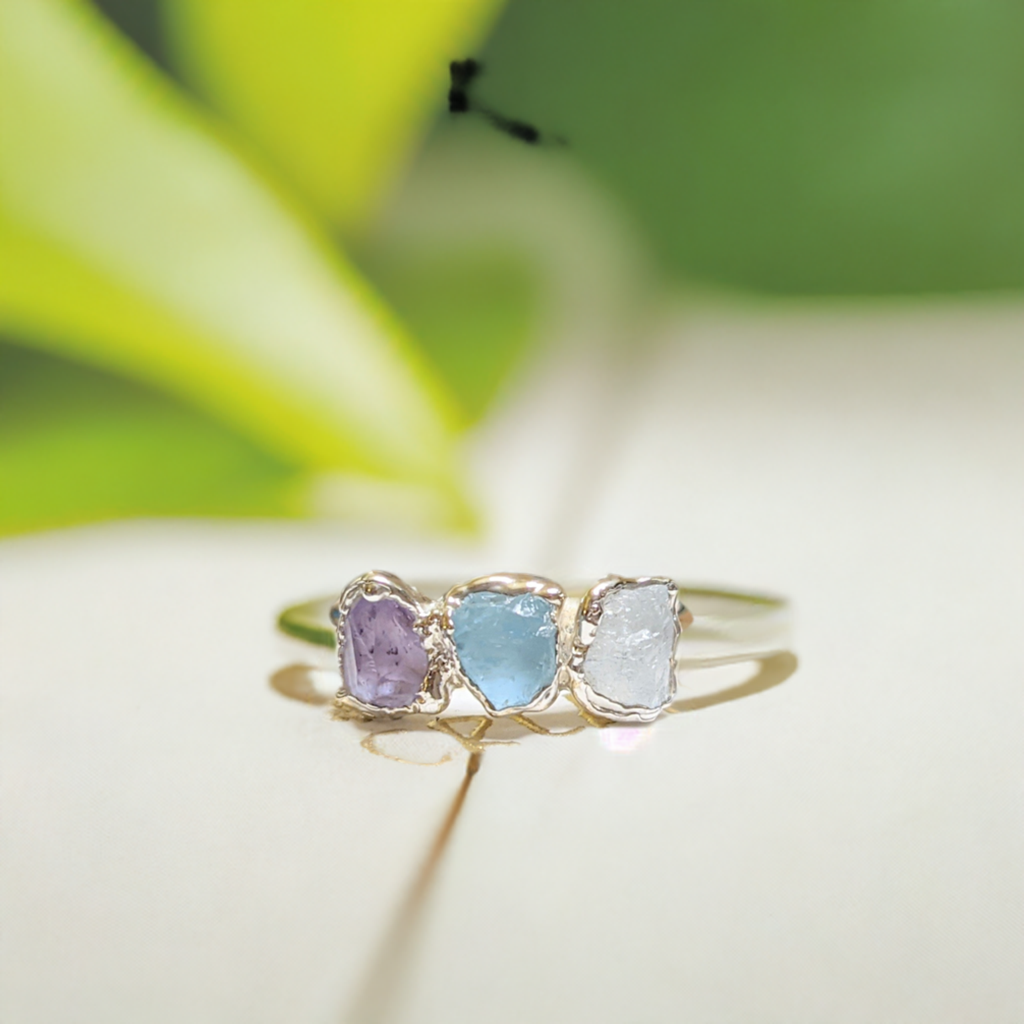 Handcrafted raw gemstone family birthstone ring featuring amethyst, aquamarine, and moonstone on a gold band.