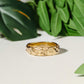 Handcrafted molten gold wedding ring featuring a rustic textured design, surrounded by green leaves.