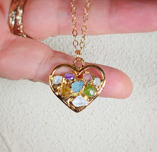 Heart-shaped gold necklace with colorful birthstones representing family members, held in hand.