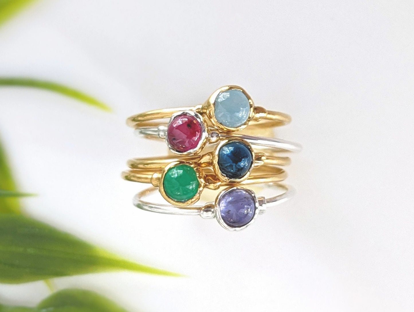 Stack of colorful gemstone stacking rings in gold and silver featuring ruby, sapphire, emerald, and amethyst.
