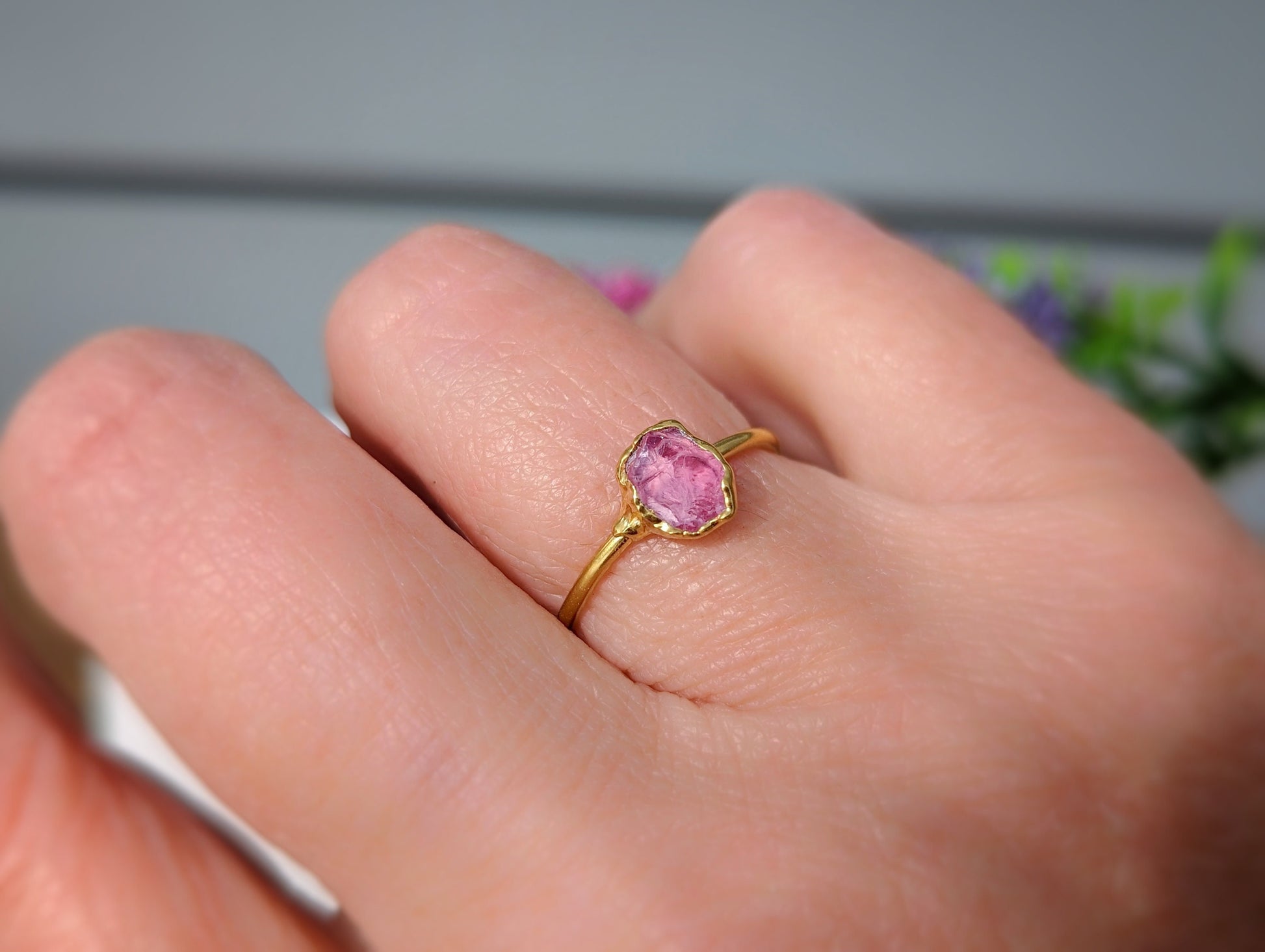 Raw pink spinel ring on a hand, showcasing its natural, unpolished crystal beauty and gold band.