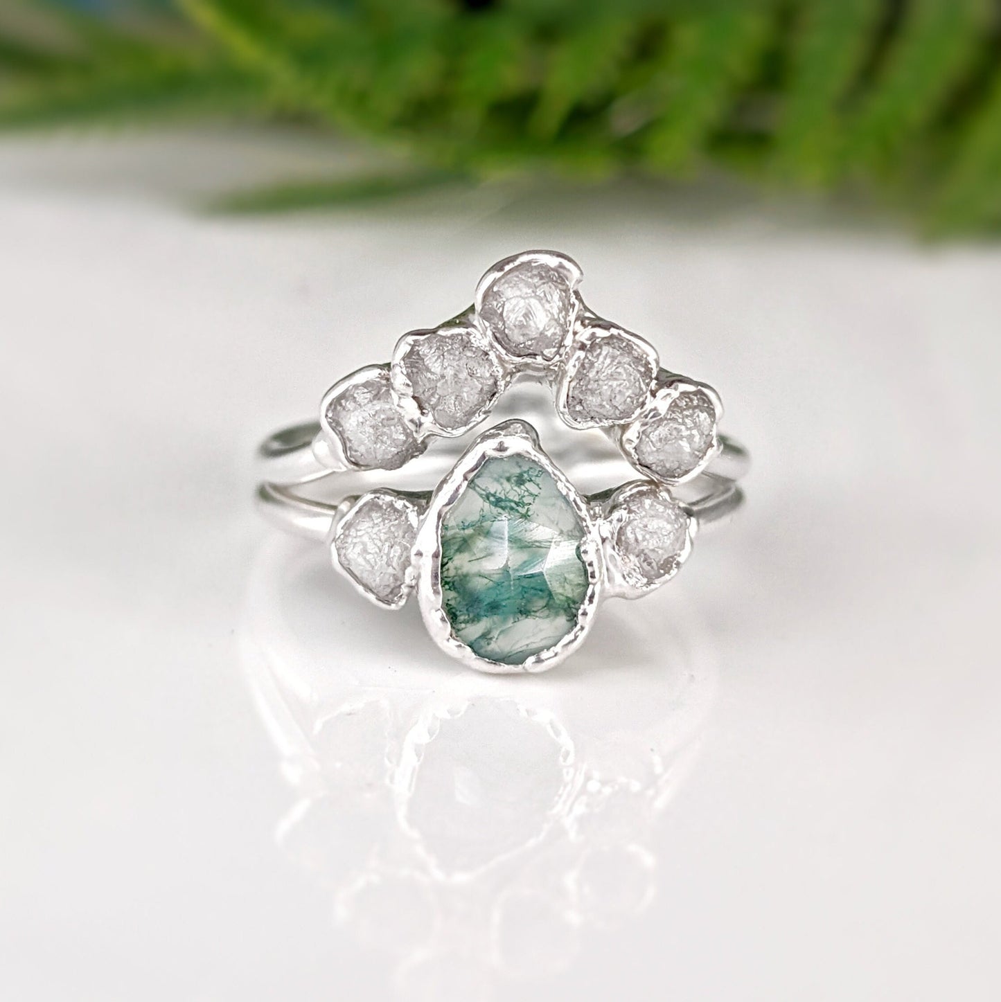 Moss Agate and raw diamond bridal ring set on a polished surface with green background.