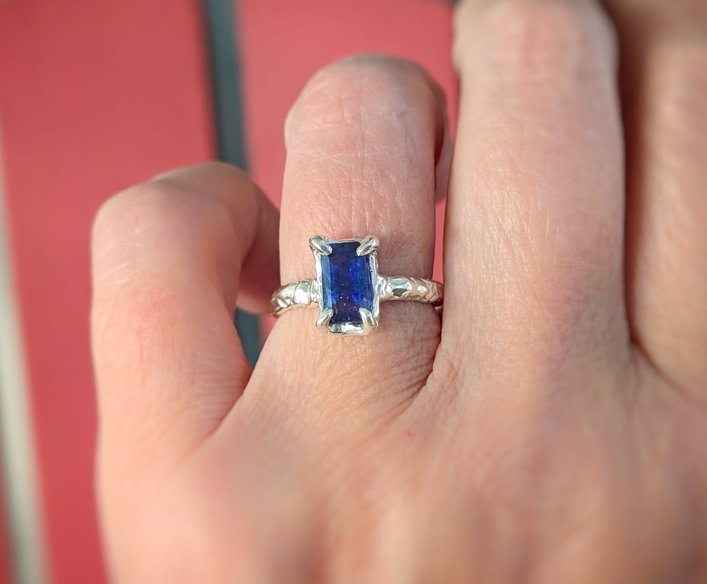 Elegant blue sapphire cocktail ring in solid 14k gold, featuring a unique emerald cut and textured band.