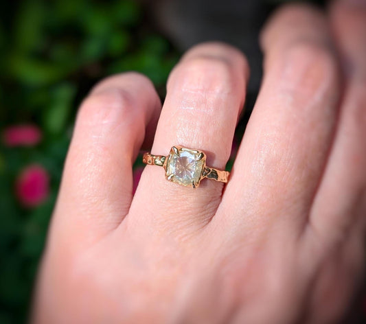 Moissanite engagement ring in 14k gold on hand, featuring an 8mm cushion cut stone and textured band.
