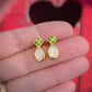 Gold stud earrings with green Peridot and opal stones held in a hand against a red background