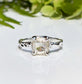 Cushion cut Moissanite engagement ring in textured silver setting with natural greenery in the background.