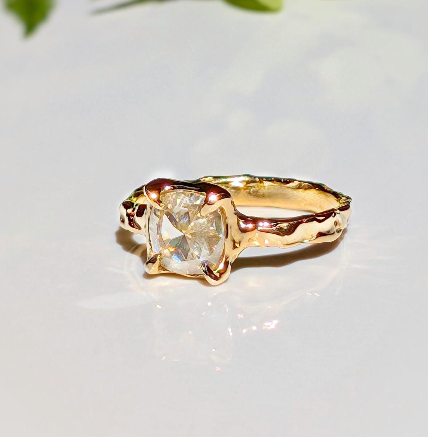 Moissanite engagement ring in solid 14k gold with a cushion cut gemstone and textured band.