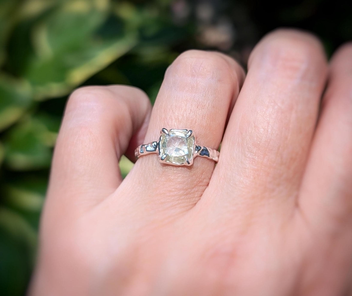 Moissanite engagement ring with cushion cut stone, set in elegant silver band, showcasing timeless beauty outdoors.