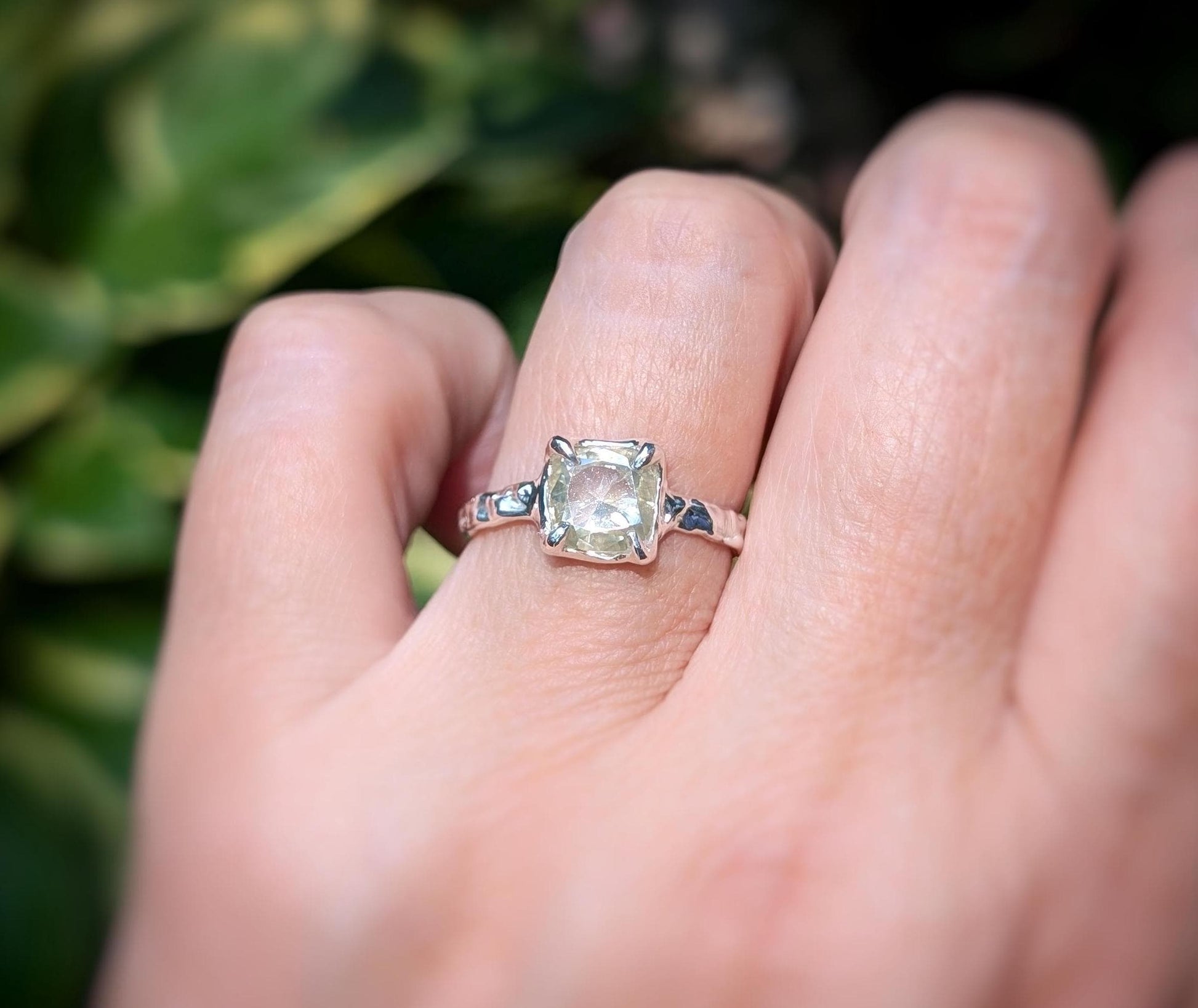 Moissanite engagement ring with cushion cut stone, set in elegant silver band, showcasing timeless beauty outdoors.