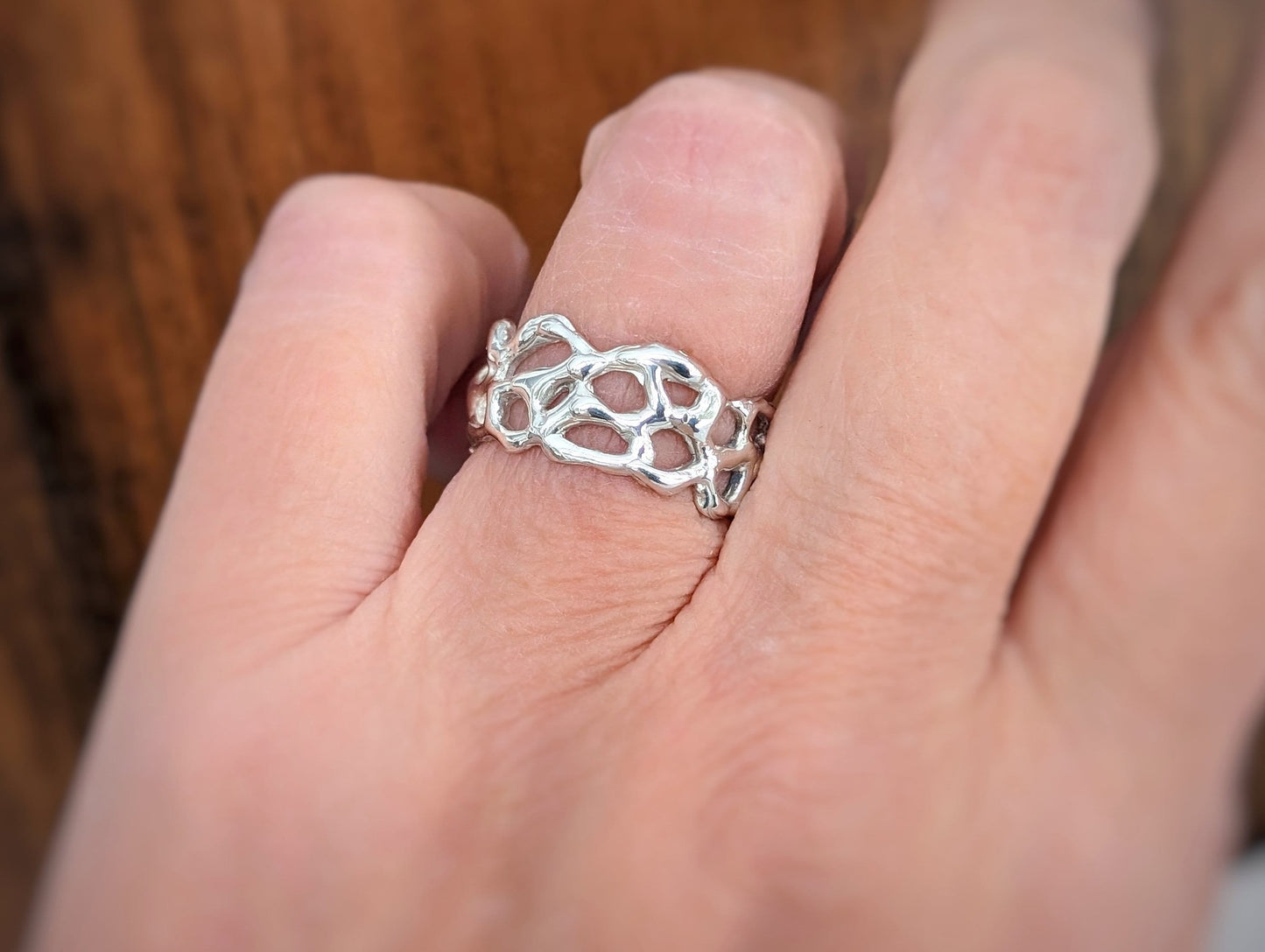 Close-up of a hand wearing a Molten Gold Honeycomb ring, showcasing its unique, nature-inspired design and abstract form.