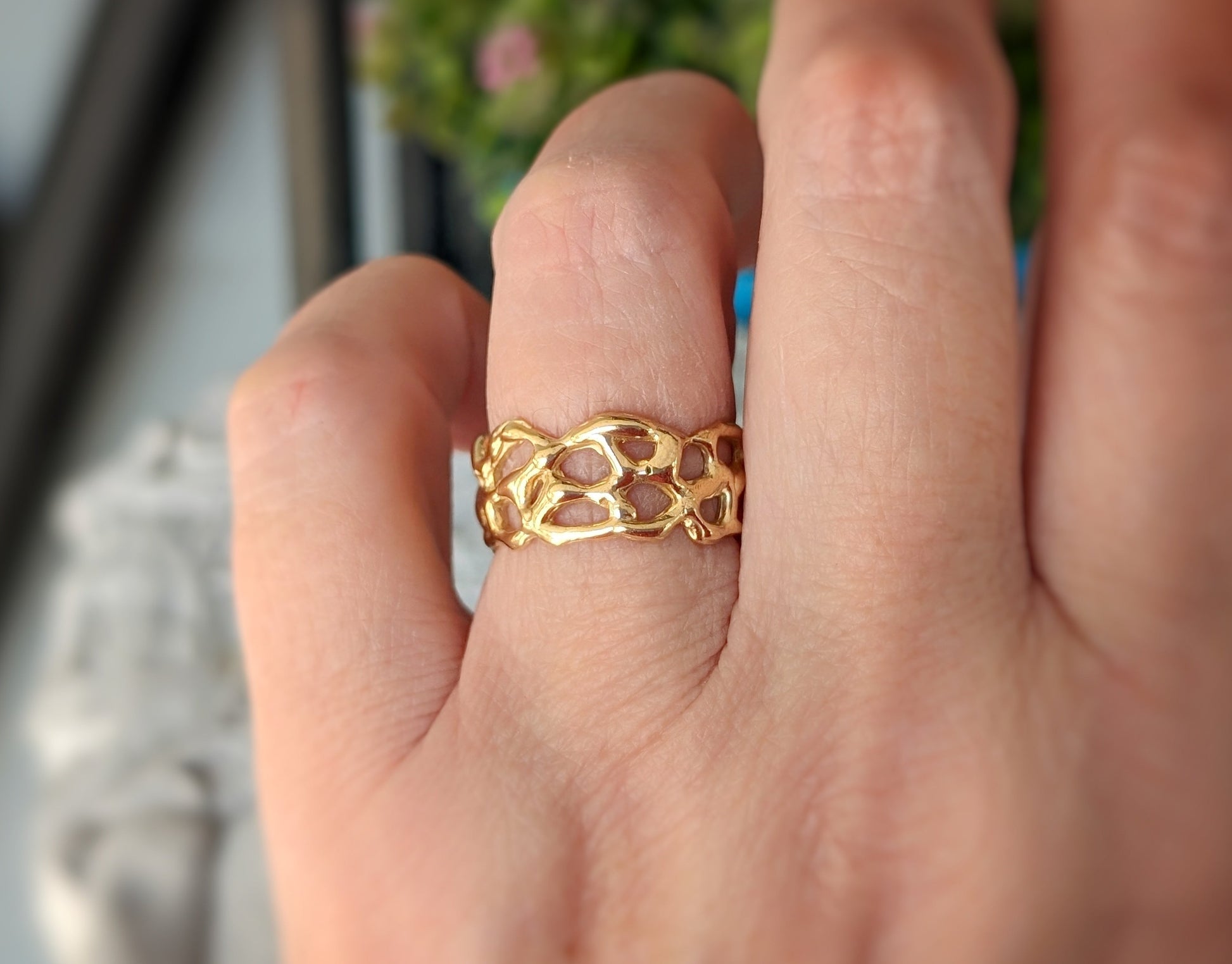 Hand wearing a unique gold honeycomb ring, showcasing its intricate design and natural aesthetic in a close-up view.