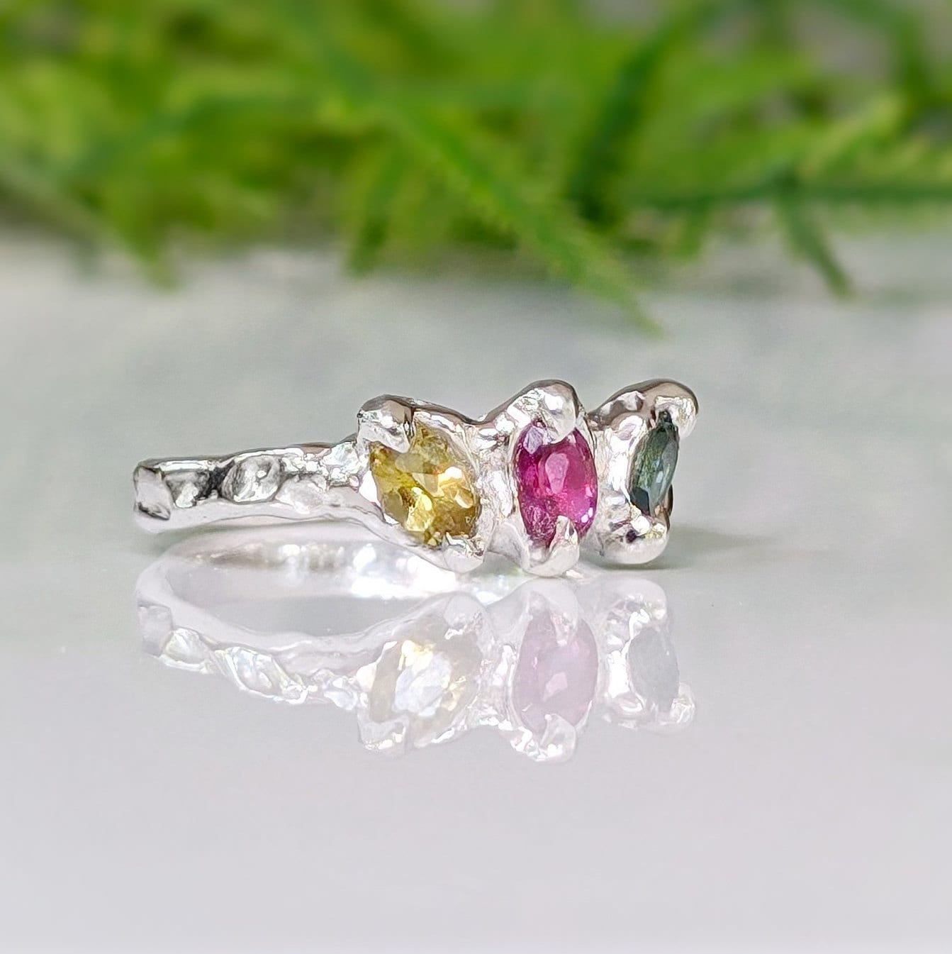 Natural multi Tourmaline silver ring with pink, green, and yellow gemstones on a reflective surface.