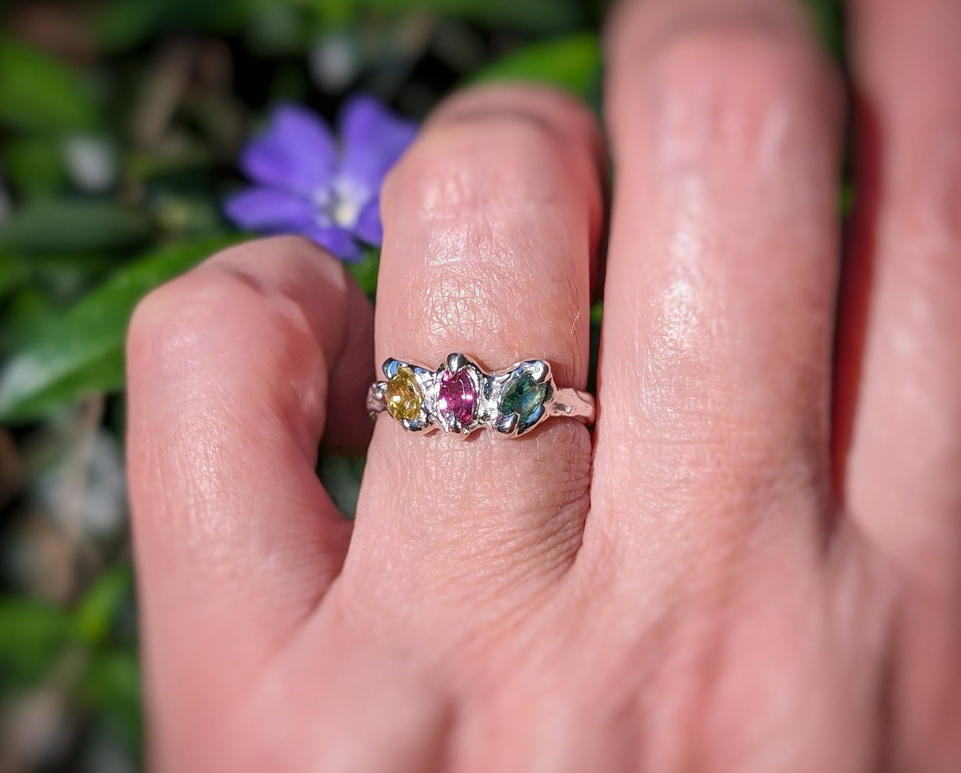 Natural multi Tourmaline silver ring showcasing colorful gemstones, worn on a hand with greenery and a purple flower backdrop.