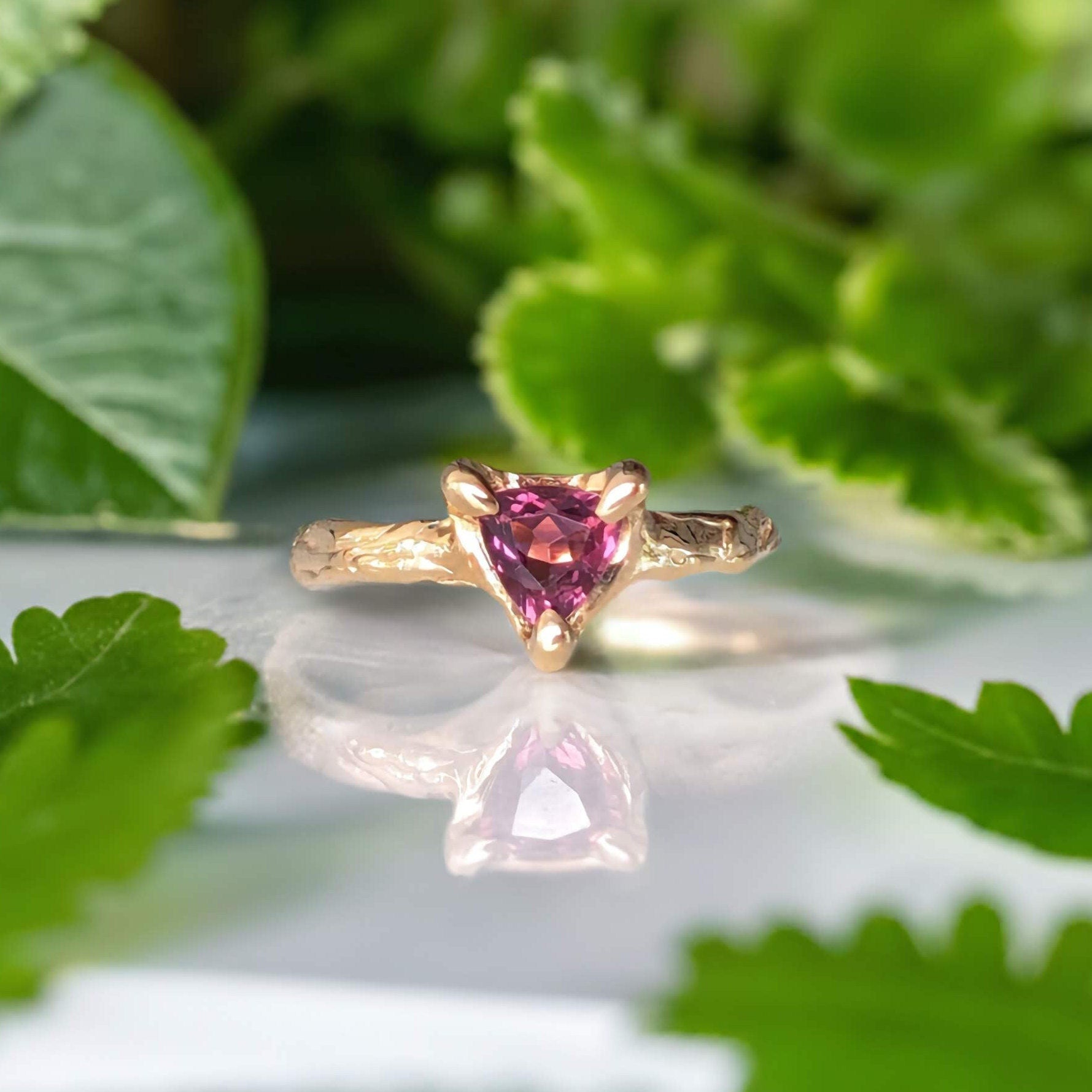 Natural Rubellite Tourmaline ring in gold featuring a triangle-cut stone, surrounded by green foliage.