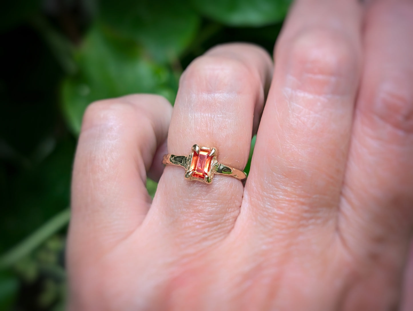 Hand wearing a radiant cut Orange Sapphire textured ring in Solid 14k Gold, showcasing a unique engagement ring design.