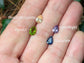 Hand holding gemstones: Peach Morganite, Peridot, Amethyst, and Sapphire in vibrant colors.