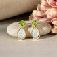Gold earrings with green Peridot and Opals on a stone surface with pink flowers in the background