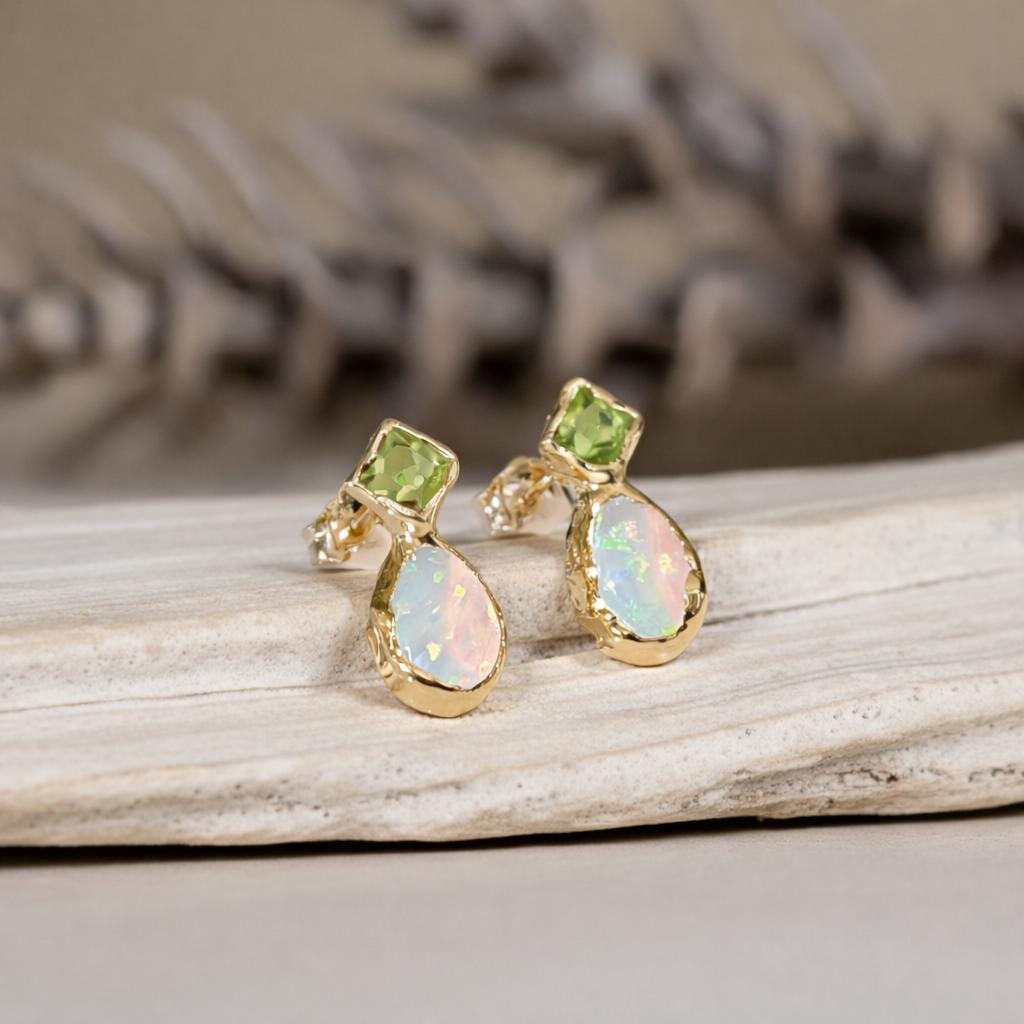 Gold stud earrings with green Peridot and opal stones on a wooden surface
