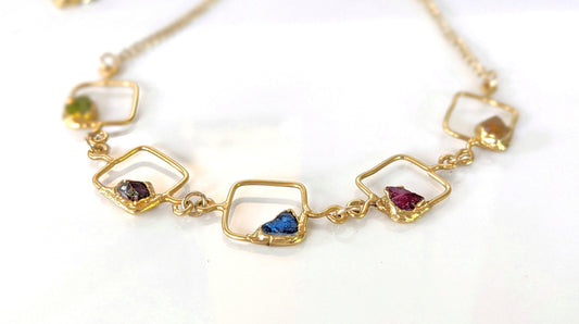 Close-up of personalized family birthstone necklace with raw gemstones and gold accents on square pendants.
