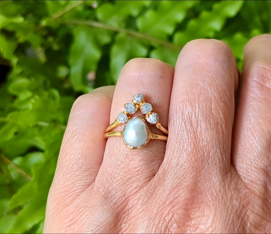 Freshwater pearl and raw diamond chevron wedding ring set in solid 14k gold on a hand, surrounded by greenery.