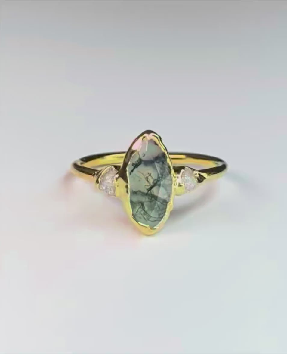 Gold Moss Agate and raw diamond engagement ring in a light background with some greenery