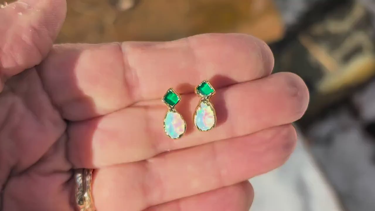 Hand holding a pair of Emerald and Opal stud earrings in Gold finish