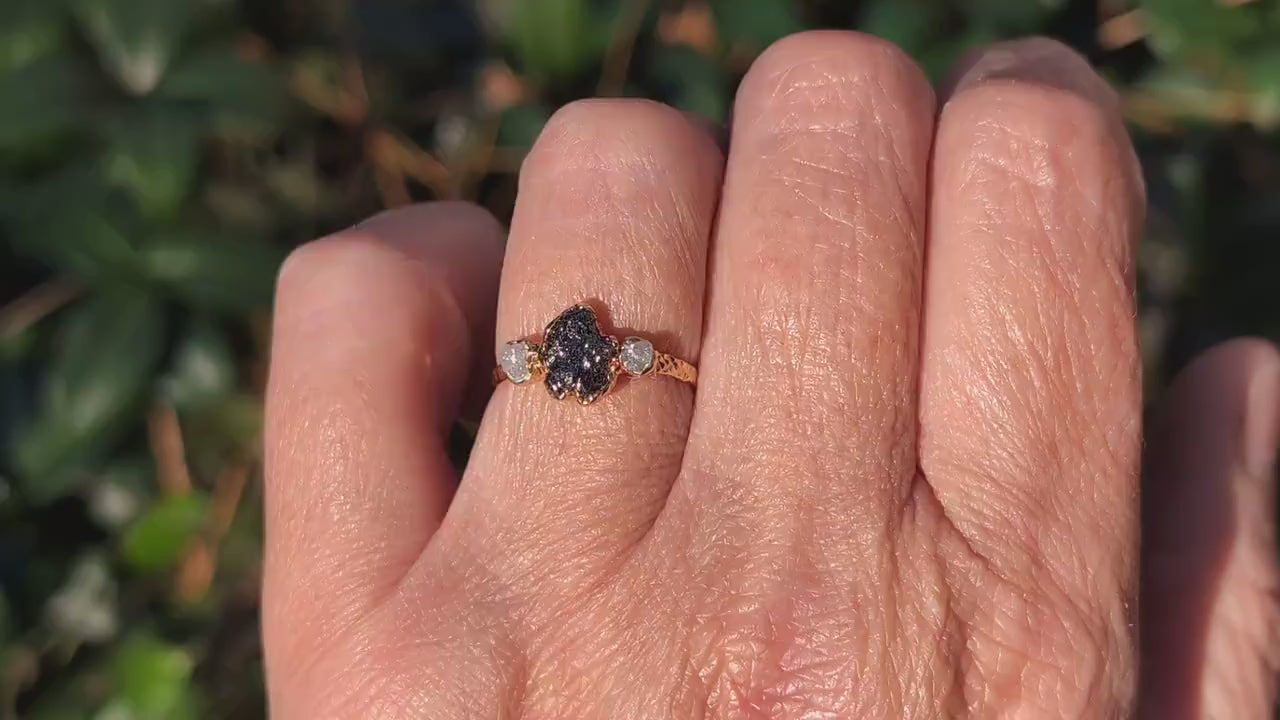 Raw uncut Black Diamond engagement ring on hand, featuring two smaller raw diamonds and a 14k Gold band.