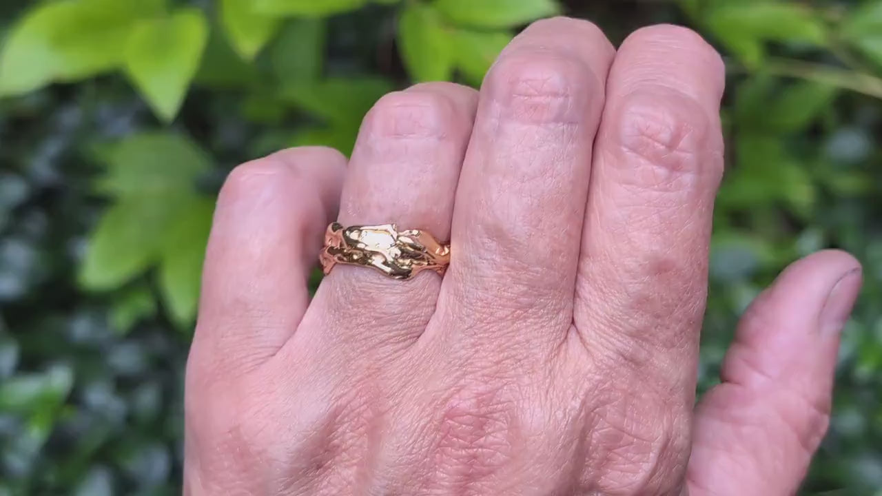 Hand wearing a textured molten gold wedding ring with abstract design, set against a leafy background.