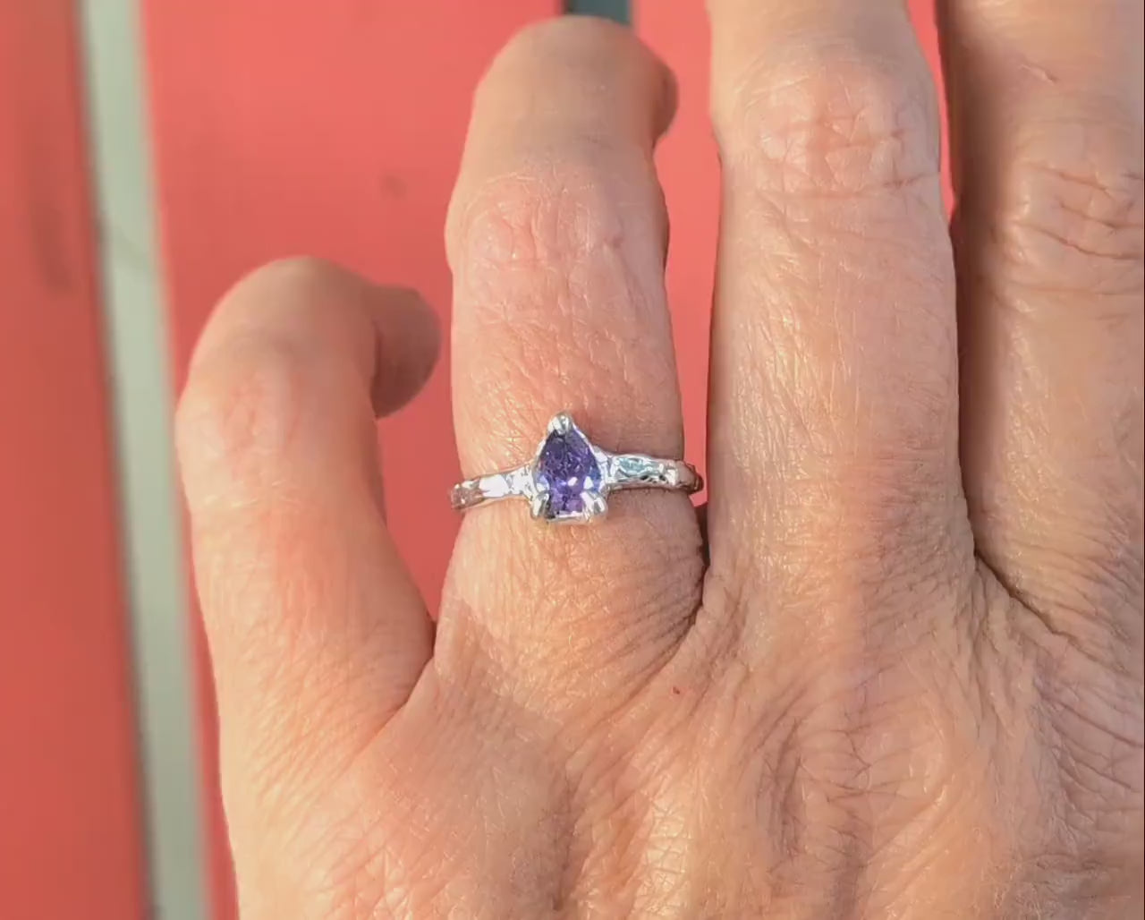 Hand showing a handcrafted Amethyst engagement ring in solid sterling silver with an organic textured band.