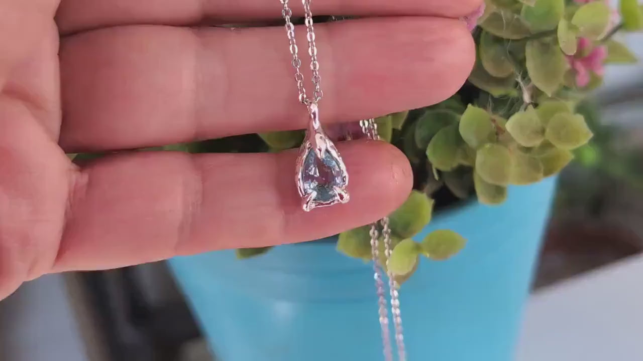 A hand holding a Silver Aquamarine necklace