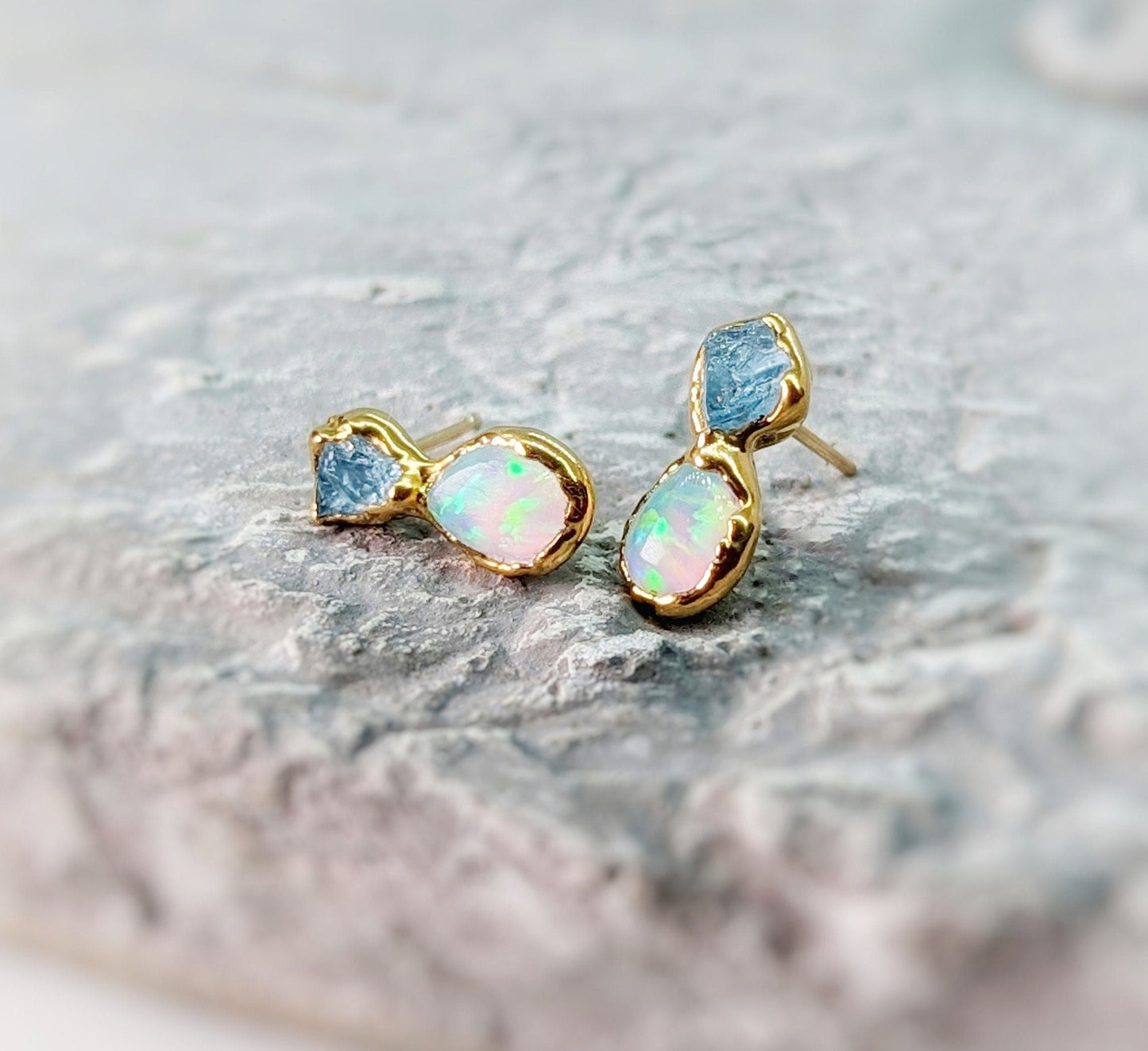 Dainty raw Aquamarine and Opal stud earrings with gold accents on a textured background, elegant and handcrafted.