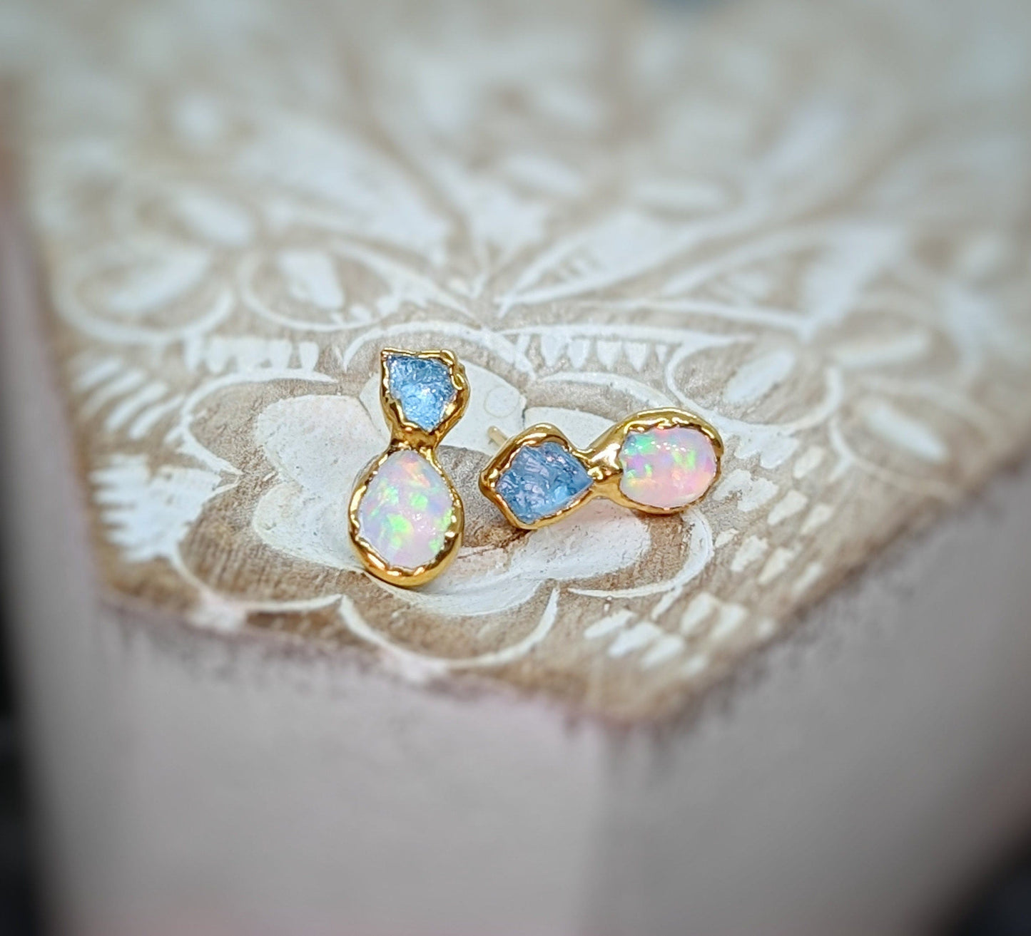 Dainty raw Aquamarine and Opal stud earrings with gold settings on a rustic background.