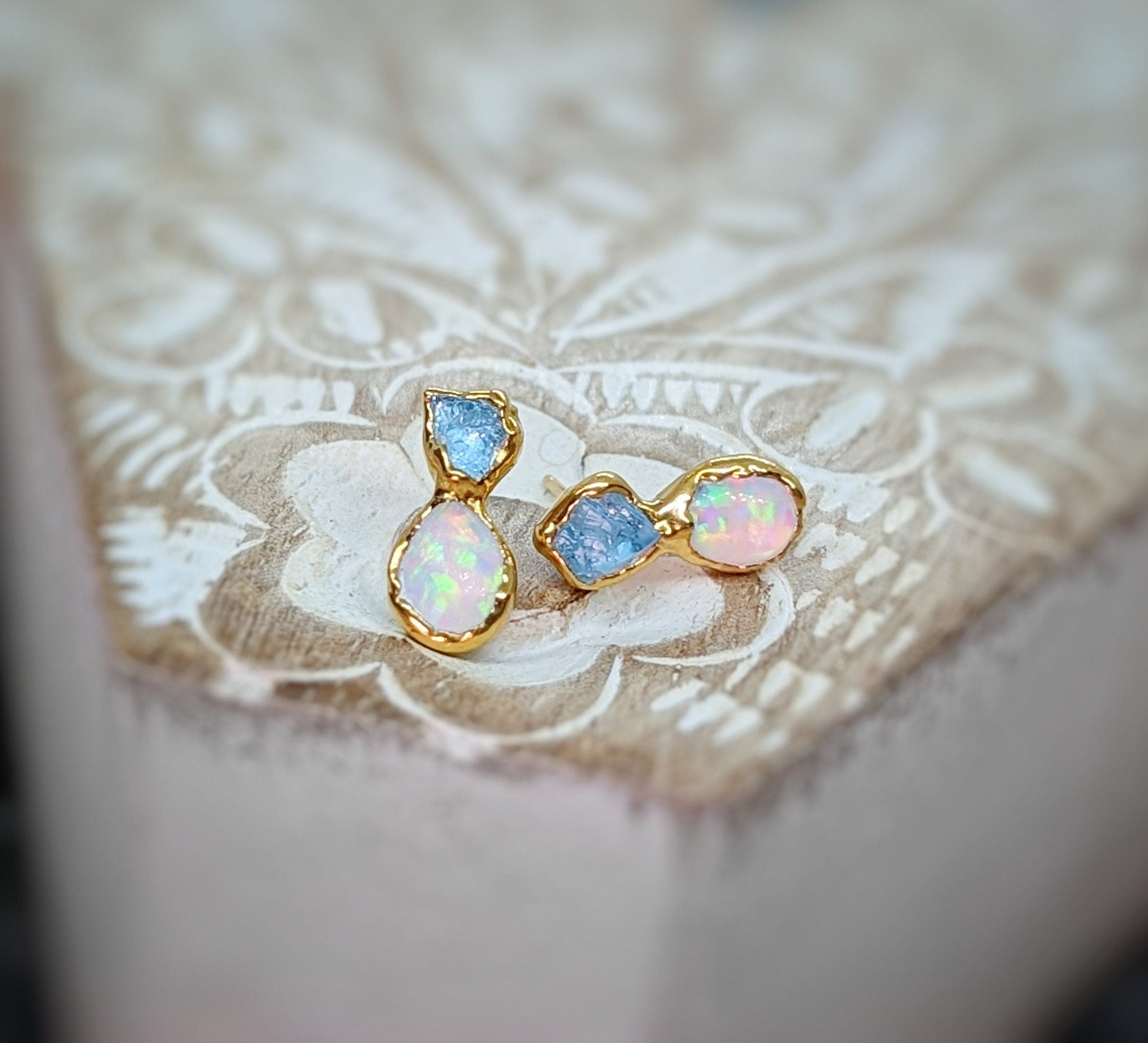 Dainty raw Aquamarine and Opal stud earrings with gold settings on a rustic background.