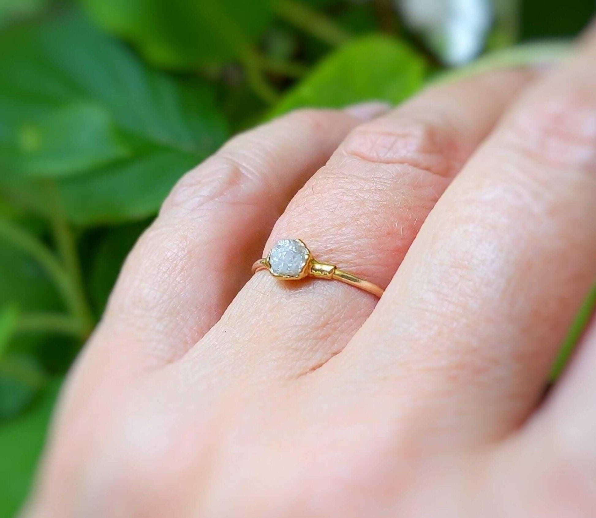 Raw diamond engagement ring on hand, set in solid 14k gold band amidst greenery.