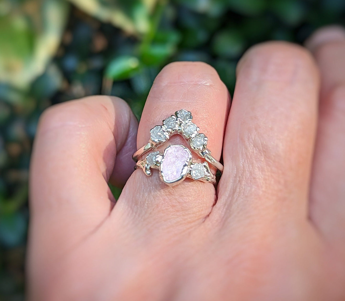 Hand wearing a pink Morganite and raw diamond ring against a blurred green background