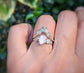 Hand wearing a pink Morganite and raw diamond ring against a blurred green background