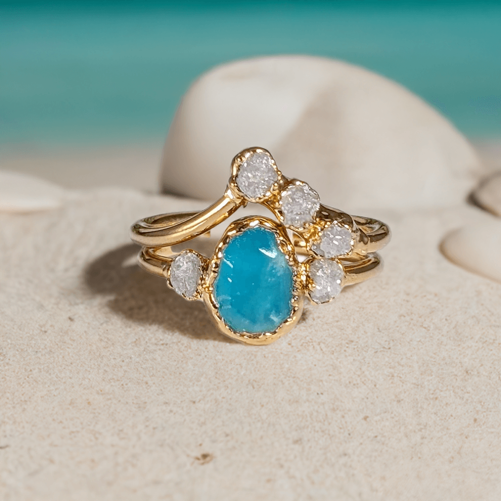 Raw Peruvian Opal and diamond engagement ring set on sandy beach, showcasing unique aqua-blue opal and sparkling diamonds.