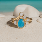Raw Peruvian Opal and diamond engagement ring set on sandy beach, showcasing unique aqua-blue opal and sparkling diamonds.