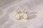 Pair of gold stud earrings with Amethysts and opal gemstones on a textured beige surface