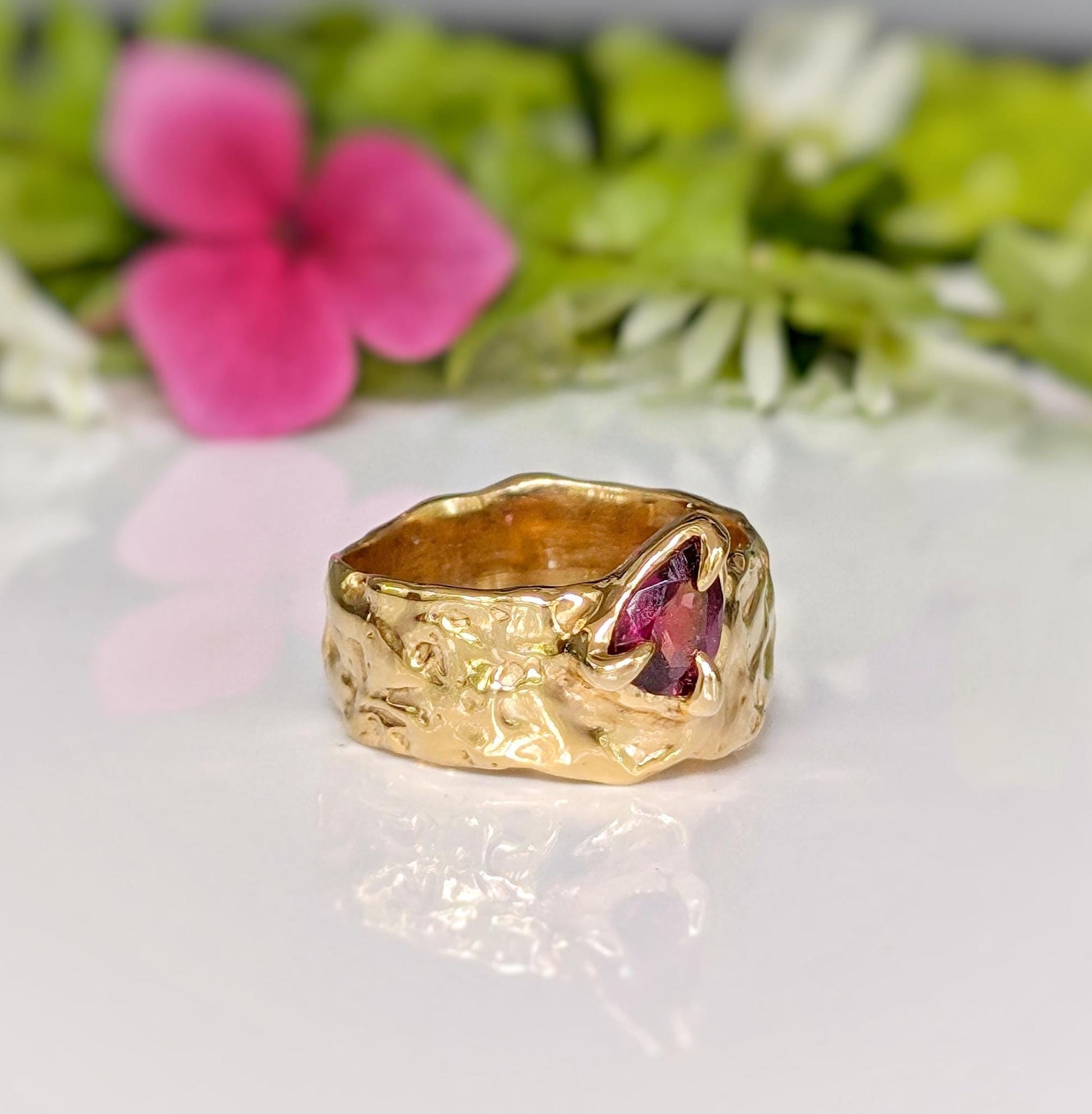 Handcrafted Rubellite Tourmaline ring in textured solid 14k gold setting against floral backdrop.