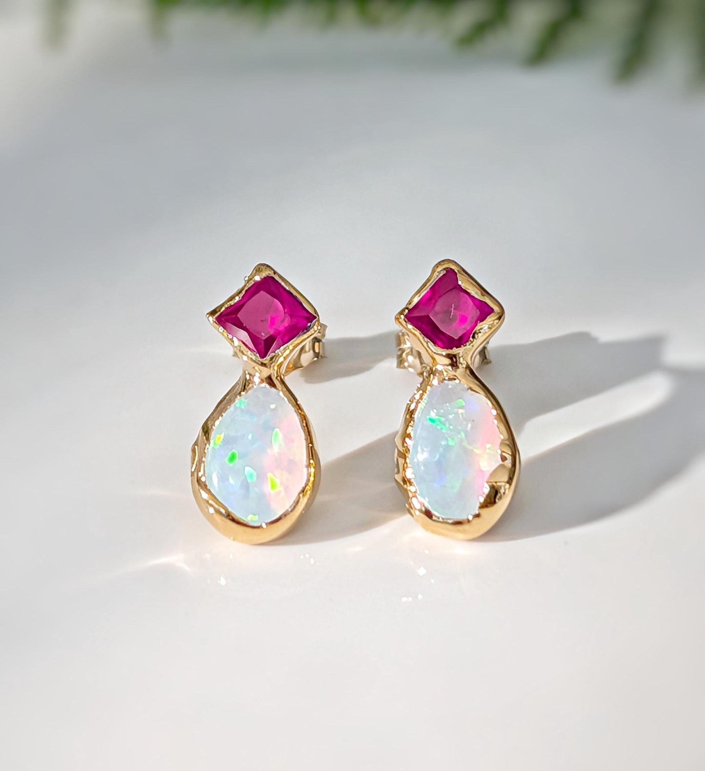 Pair of Gold stud earrings with dark pink Rubies and White Opals on a light background
