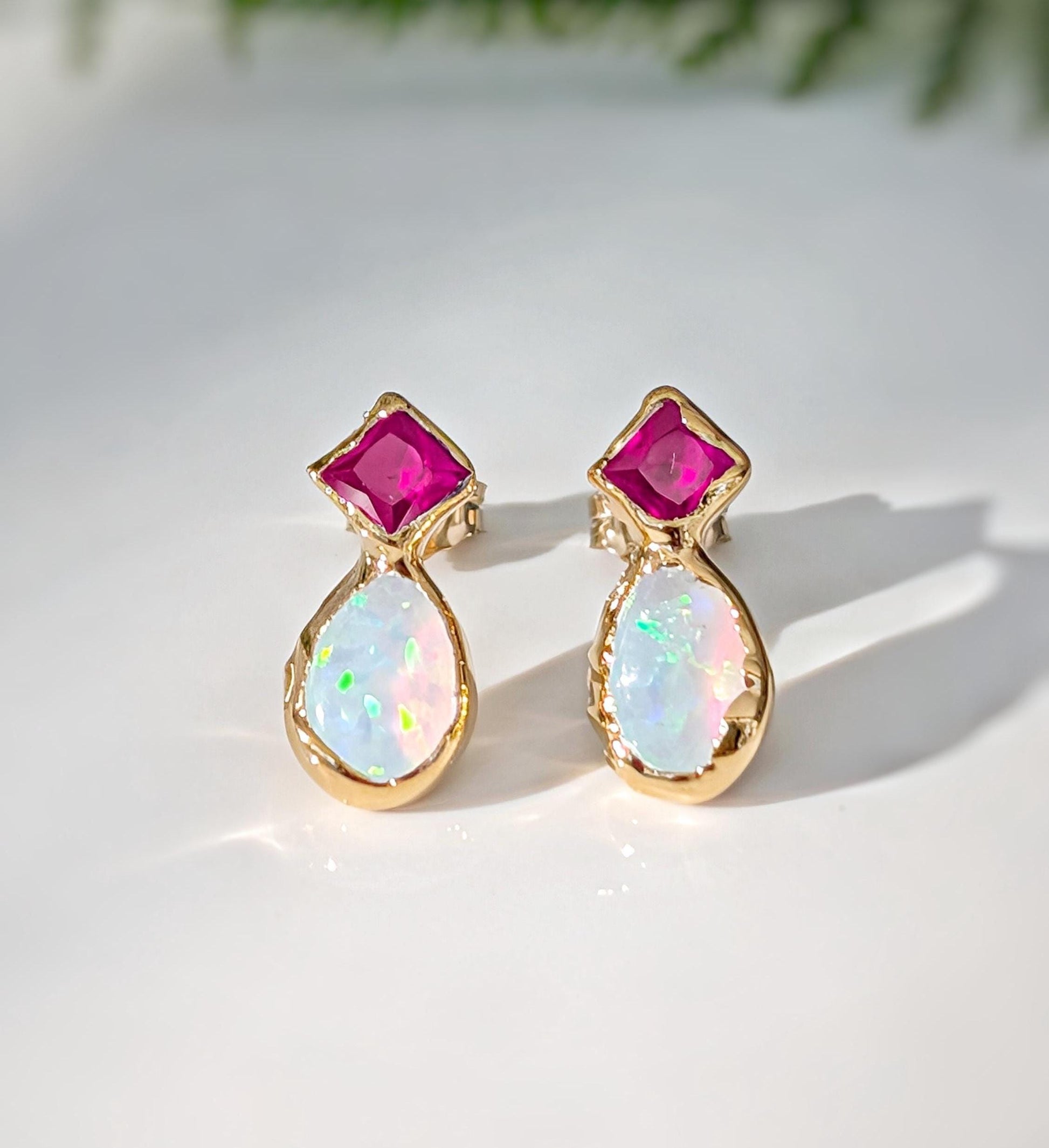 Pair of Gold stud earrings with dark pink Rubies and White Opals on a light background