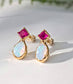Gold stud earrings with dark pink Ruby and white Opal gemstones on a light background