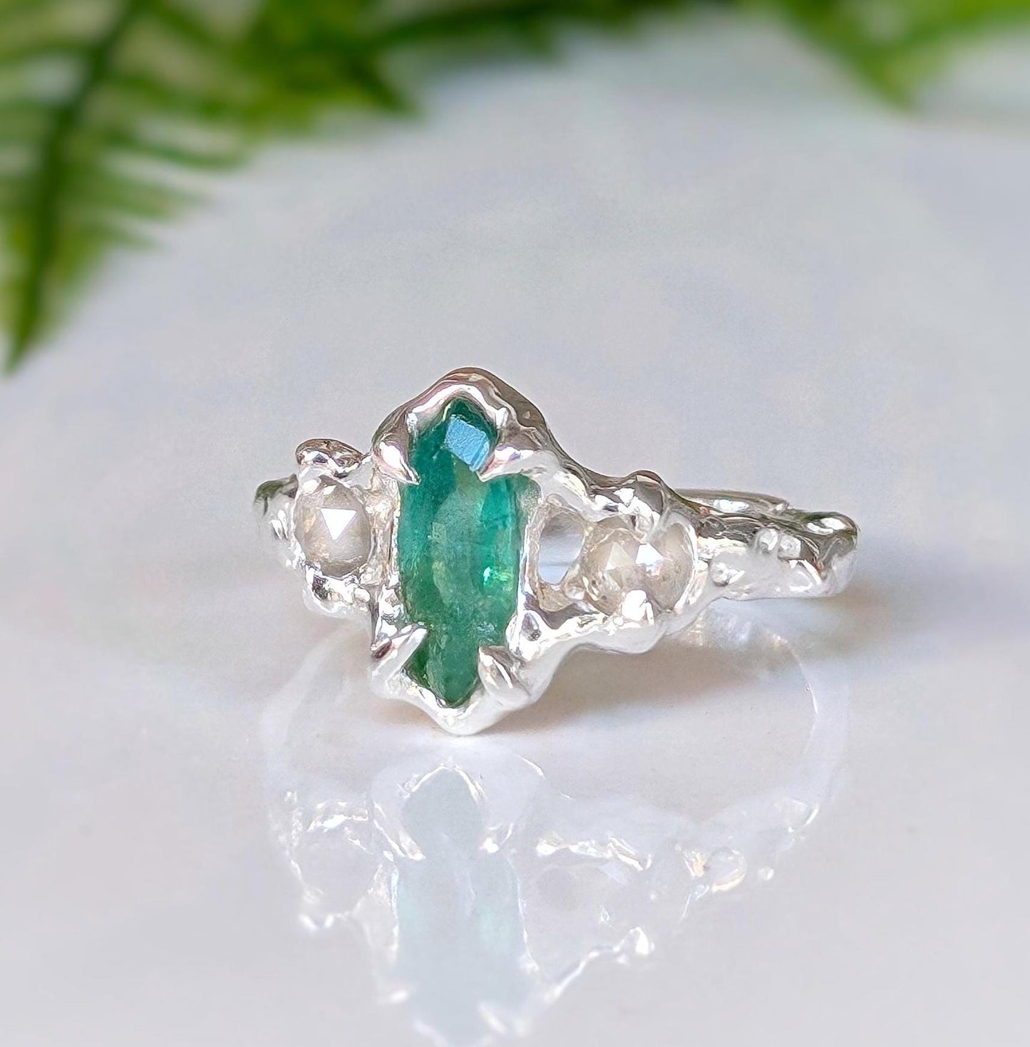 Hand-carved silver engagement ring featuring a marquise cut emerald and salt & pepper diamonds, nature-inspired design.