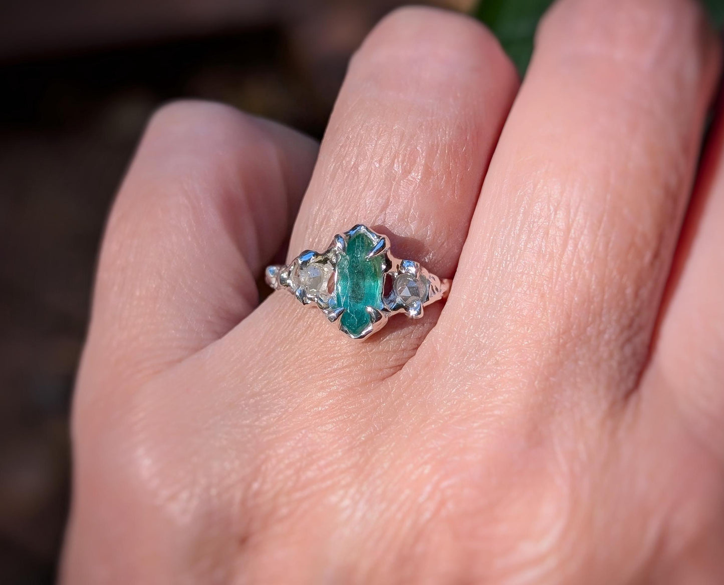 Silver engagement ring featuring a marquise cut emerald and salt & pepper diamonds on a hand.