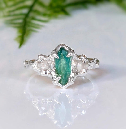 Silver emerald and diamond engagement ring with marquise cut emerald and textured band.