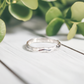 Handcrafted Molten Silver wedding band featuring an irregular abstract form on a wooden surface with greenery.