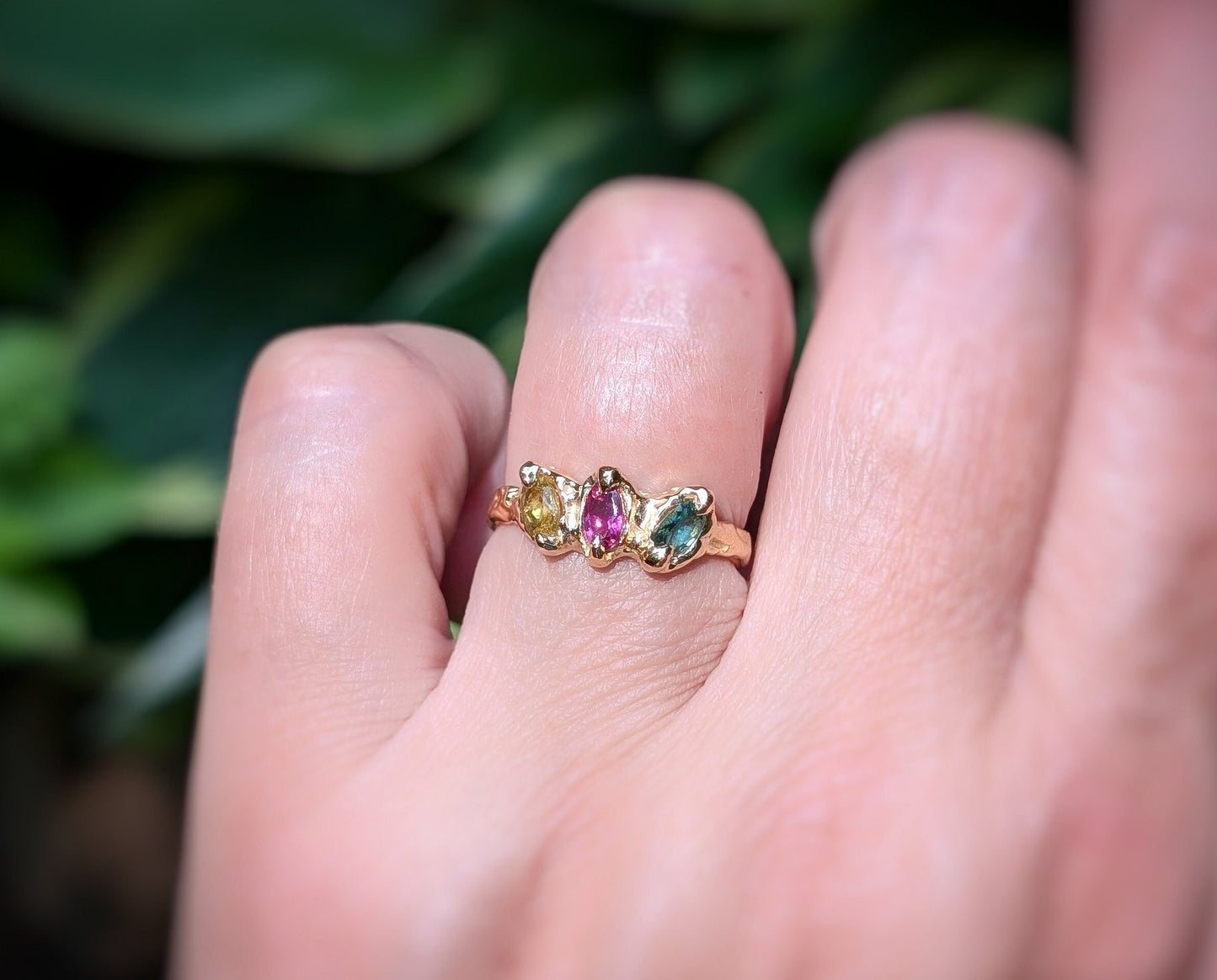 Solid gold multi Tourmaline ring featuring three colorful gemstones on a hand against a natural background.